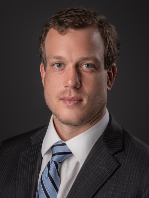 Will Platt looks at the camera wearing a blue striped tie and dark suit