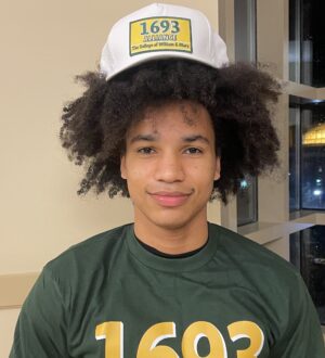 Colin Ndaw smiles at the camera wearing a 1693 Alliance hat and t shirt