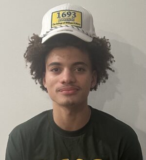 Kyle Pulliam smiles at the camera wearing a 1693 Alliance shirt and baseball cap