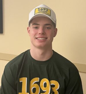 Luke Kinkade smiles at the camera wearing a 1693 shirt and white baseball cap