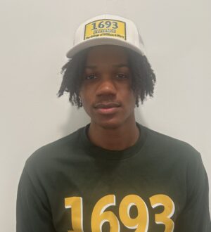Miles Hicks looks at the camera wearing a green 1694 Alliance shirt and white baseball hat